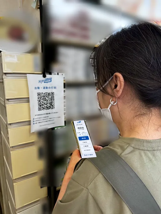 お店の棚に掛けた「出勤・退勤の打刻」のQRコードを、女性がスマホで読み、打刻の画面を開いている