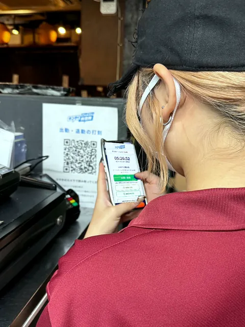 お店に貼った打刻用のQRコードのそばで、スタッフがスマホで LINE の打刻の画面を開いている